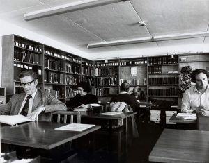 Black and white photograph of the archive searchroom with several researchers sitting at desks looking at archival documents