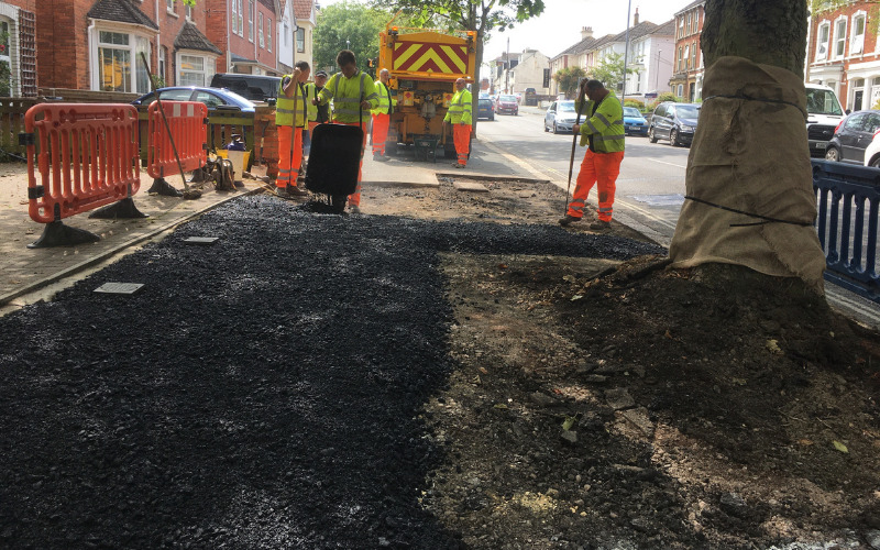 workers hand laying new pavement bitumen surface around tree area