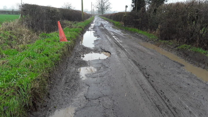 looking down a rural minor road that has many water-filled potholes