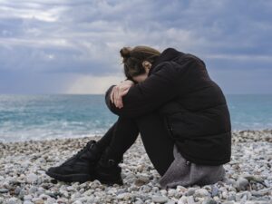 illustrative image of woman by the sea looking down at her knees