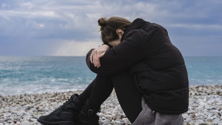 illustrative image of woman by the sea looking down at her knees