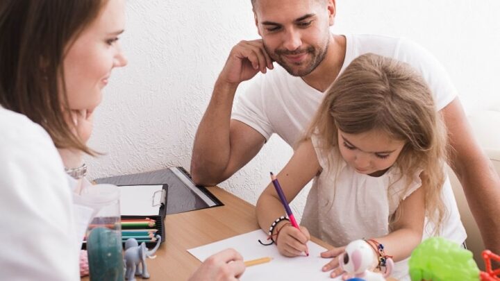 A man and a woman are looking at a young girl who is writing something