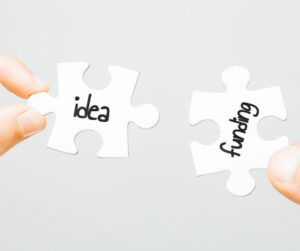 A photograph of two pieces of a puzzle joining with the labels 'idea' and 'funding'