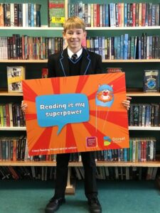 A photo of hector holding up a sign that says 'Reading is my superpower!'