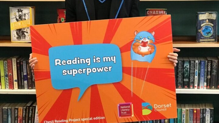 A photo of hector holding up a sign that says 'Reading is my superpower!'