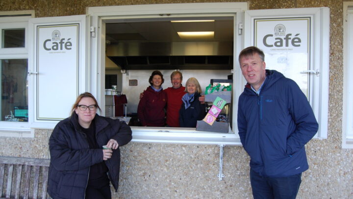 Cllr Laura Beddow and Martin Kimberley pose outside Redlands community cafe with three volunteers standing inside.