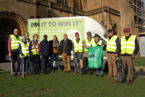 Litter pickers and Dorset Council reps standing outside Sherborne Abbey with litter picking equipment, in front of a Litter Lotto branded van