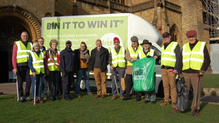 Litter pickers and Dorset Council reps standing outside Sherborne Abbey with litter picking equipment, in front of a Litter Lotto branded van
