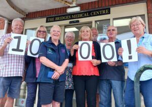 A group of people smiling at the camera holding a "1000" sign