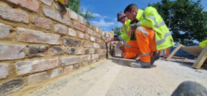 two workers in yellow jacket and orange trousers examining a wall