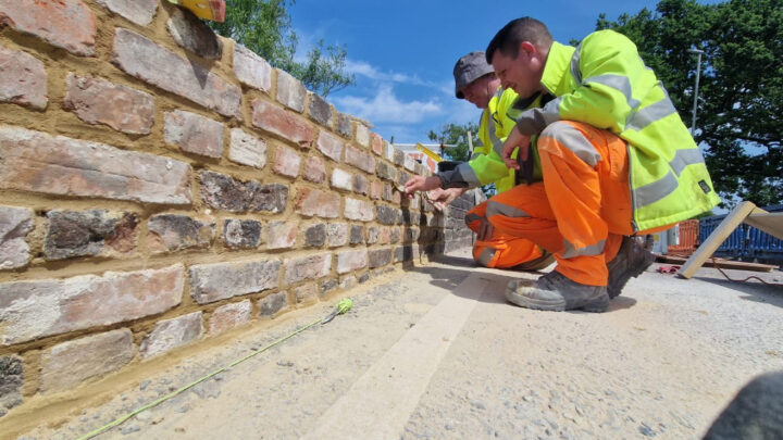 two workers in yellow jacket and orange trousers examining a wall