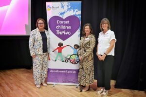 three individuals standing next to banner stand which reads 'Dorset children thrive'