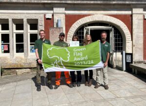 Four individuals posing for picture in front of a building holding up a Green Flag