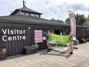 Two rangers standing in front of visitor centre building holding up green flag