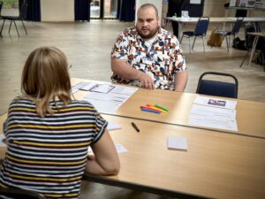 Man sat at desk talking to woman