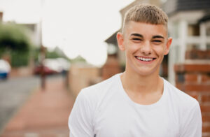 young person smiling at camera with residential street in background