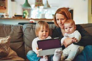woman with toddler and holding baby sitting on sofa looking at a tablet