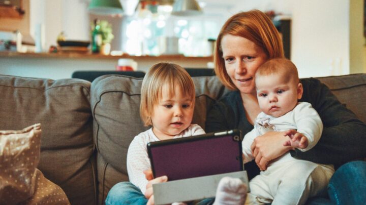 woman with toddler and holding baby sitting on sofa looking at a tablet